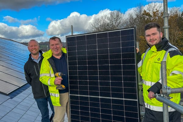 Two members of the InspireGreen team hold up a solar panel next to a client on a commercial roof during installation.