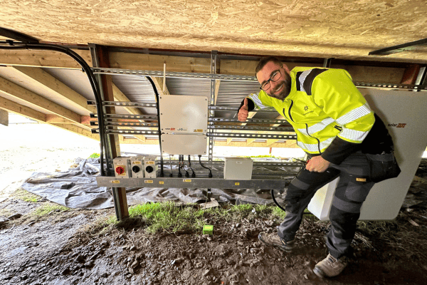 InspireGreen electrician Derry gives a thumbs up while working on a solar battery storage system underneath ground mounted panels.