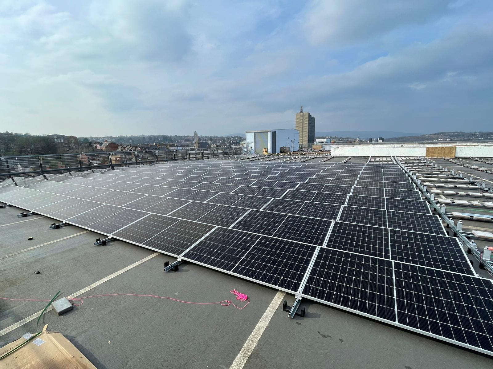 A view across rows of solar panels, installed on the top floor of a car park on a sunny day.