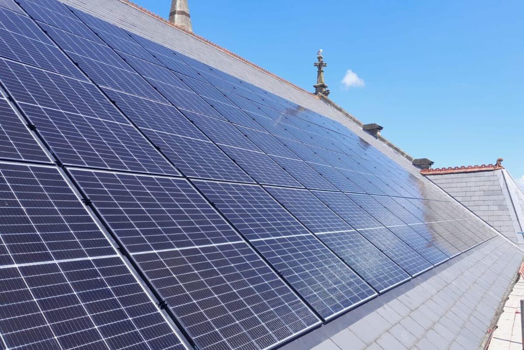 Solar panels on the side of a sloping church roof in the sun.