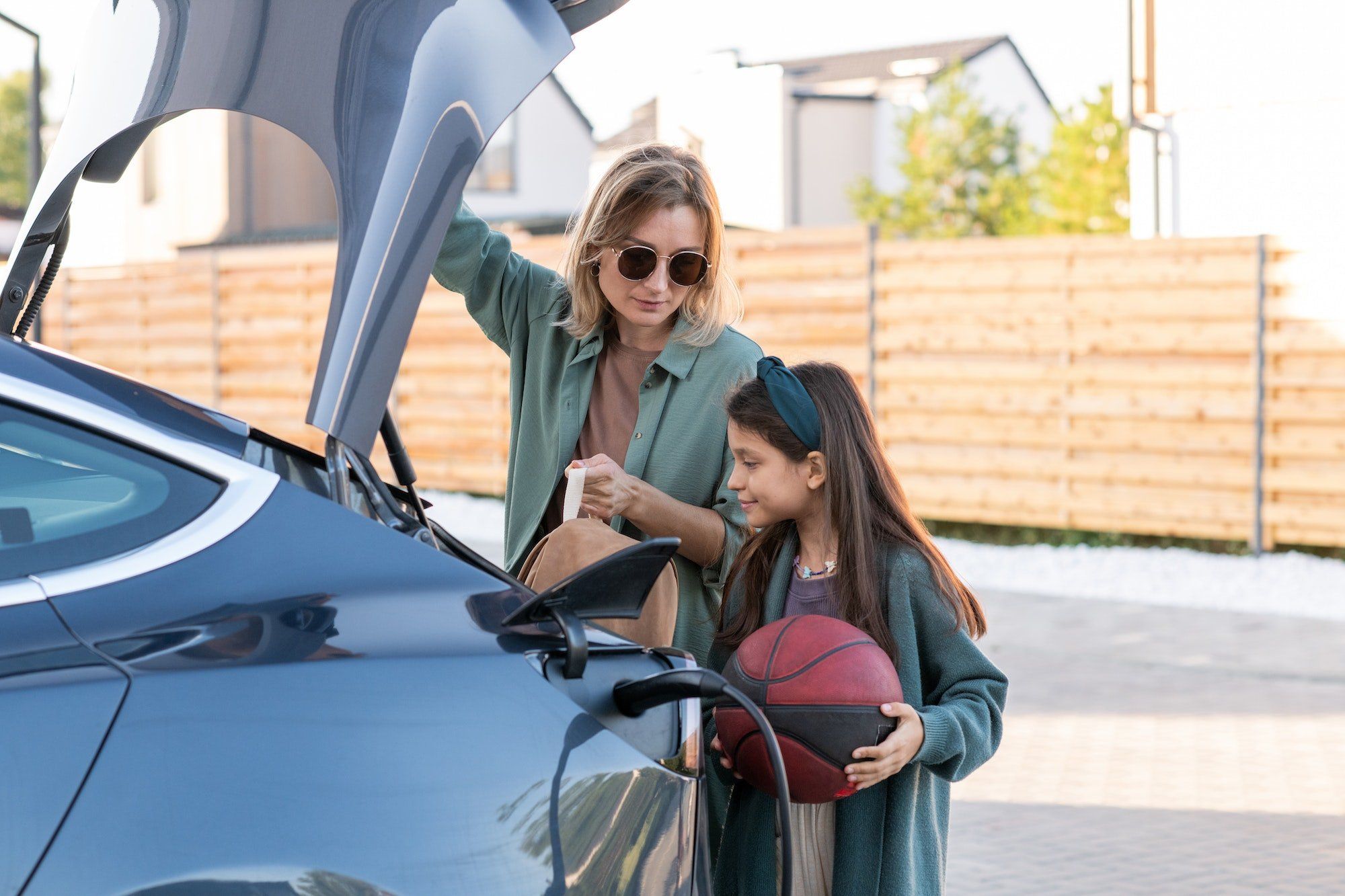 Little girl and young woman standing by trunk of electric car